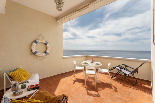 Un balcon avec une table, des chaises, un cercle de sauvetage et une vue sur la mer.