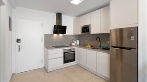 Una cucina moderna con mobili bianchi, un frigorifero in acciaio inossidabile, un forno a microonde, un forno e un lavello.