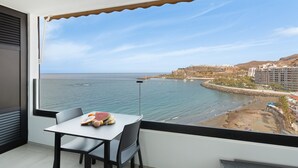 Un balcone con tavolo e sedie, affacciato su una zona costiera con edifici e una spiaggia.