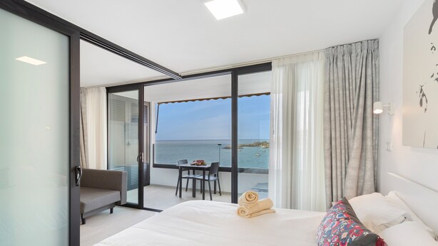 Una camera d'albergo con un letto, una sedia, un tavolo e vista mare.