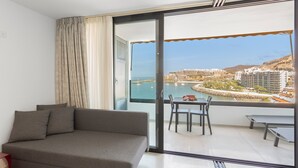 Un balcone con divano, tavolo da pranzo e sedie, affacciato su un porto turistico e edifici.