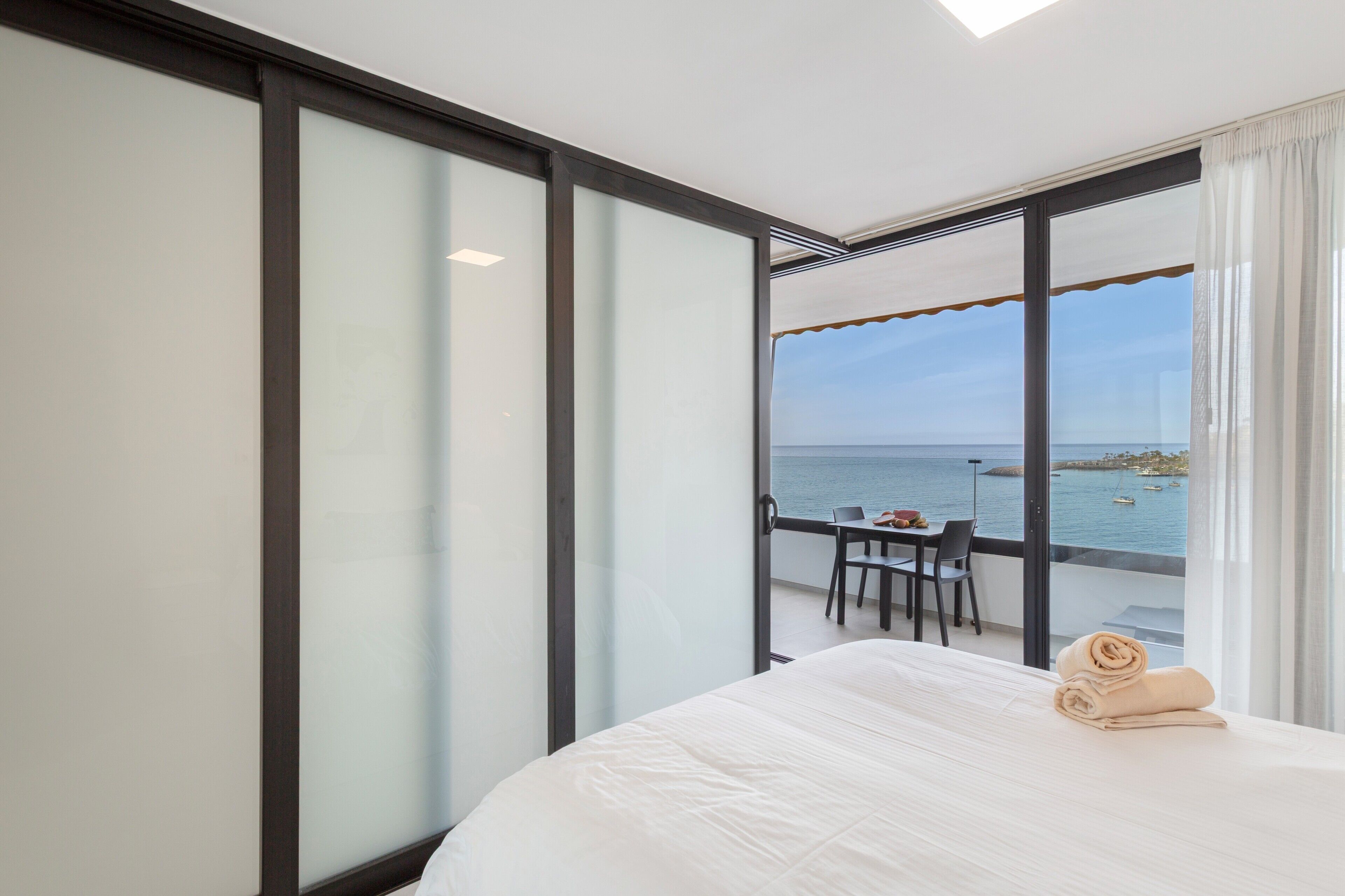 A hotel room with a bed, a table with chairs, and a view of the sea.