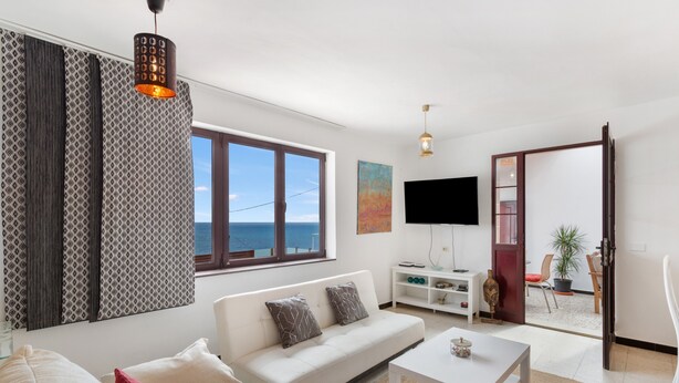 A modern living room with a sofa, coffee table, and a TV. There is a large window with a view of the sea. - Vacation Home 'Olas De Plata' with Sea View, Private Pool and Wi-Fi (Playa del Hombre)