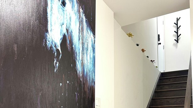 Un escalier avec des marches en bois foncé et un mur blanc orné d’un grand tableau abstrait.