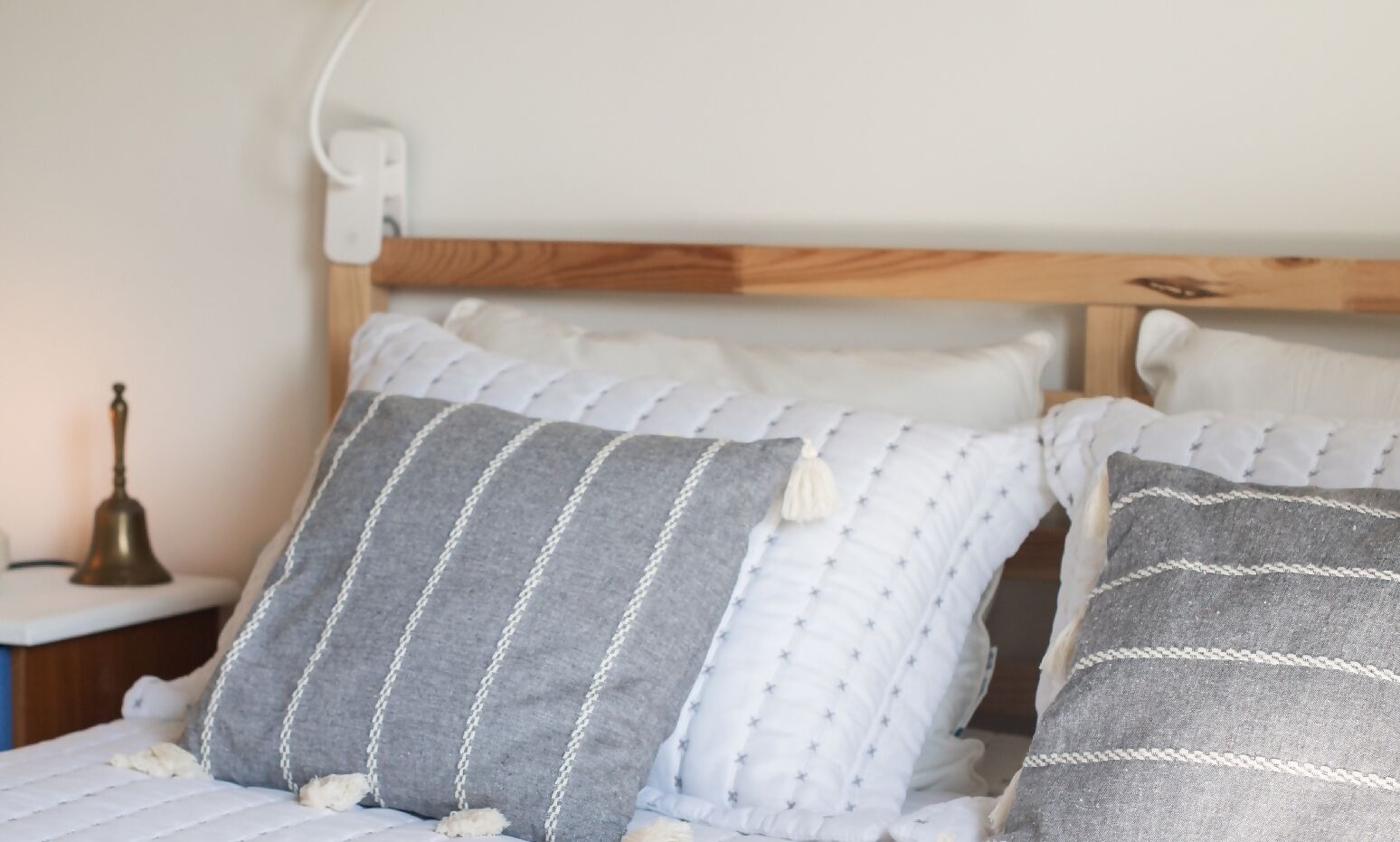 A bed with grey and white striped pillows, a wooden headboard, and a bedside table with a lamp.