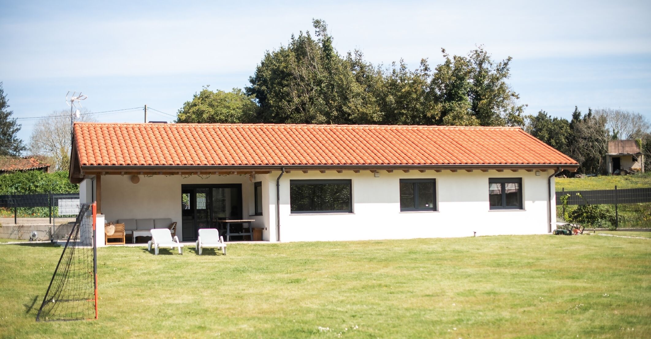 A single-story building with a red-tiled roof, a covered patio area with two white chairs, and a small table.