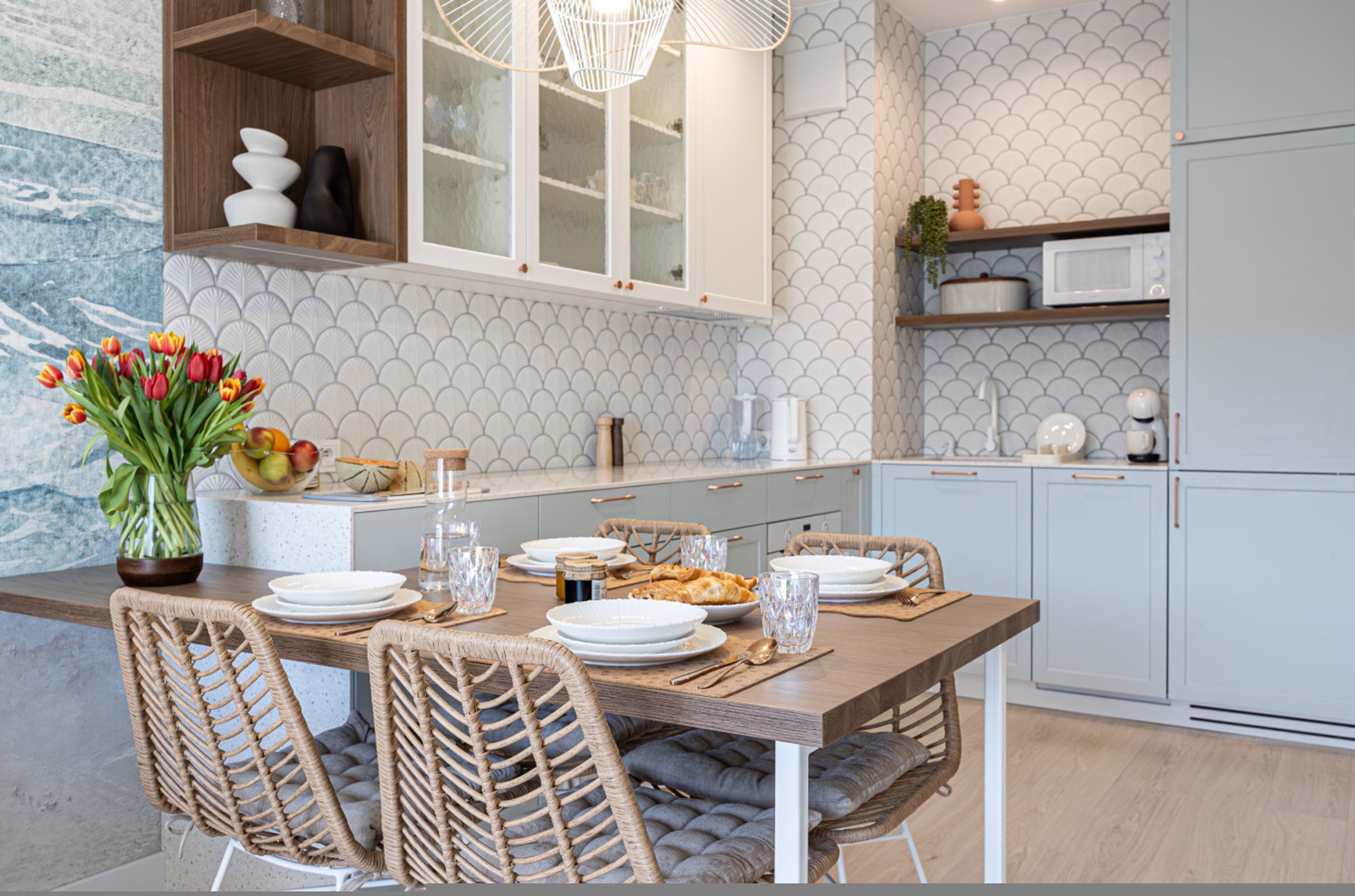 A modern kitchen with a wooden dining table, wicker chairs, and a vase of tulips.