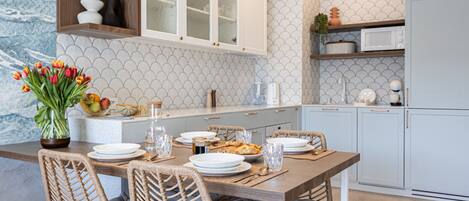 A modern kitchen with a wooden dining table, wicker chairs, and a vase of tulips.