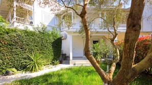 Un bâtiment blanc doté d’un balcon, entouré de haies verdoyantes et d’un arbre.