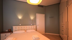 Une chambre à coucher avec un grand lit, des tables de chevet, une armoire et des luminaires fixés au mur.