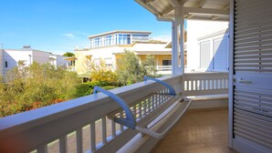 Un balcon avec une balustrade blanche, une vue sur les immeubles voisins et une porte de volet blanc fermée.