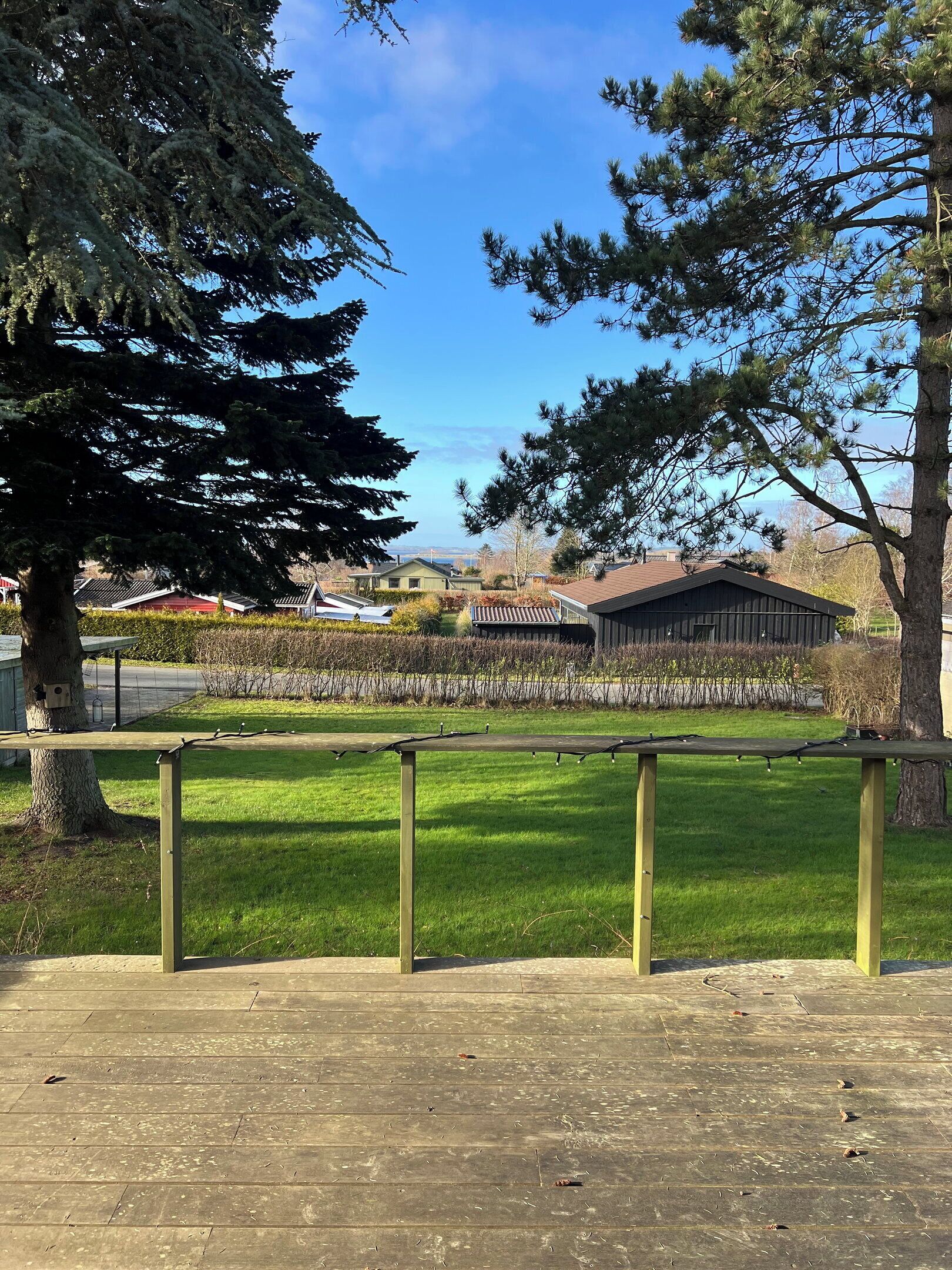A wooden deck with a metal railing, a grassy area, and a view of houses and trees in the background.