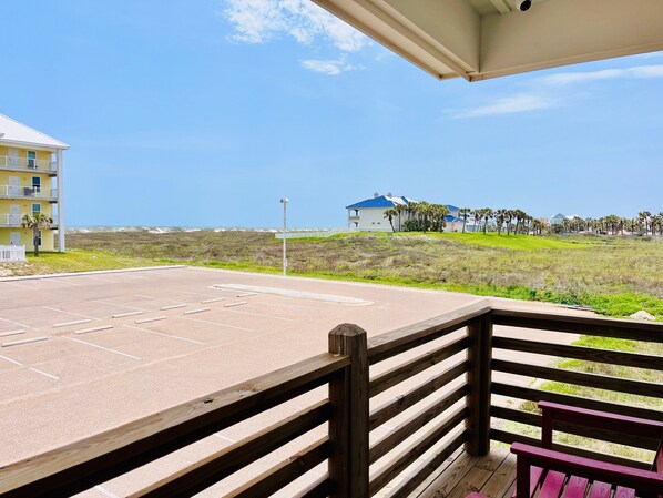 A beachfront property with a parking lot, wooden deck, and a view of the ocean and distant buildings.
