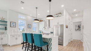 A modern kitchen with white cabinetry, a central island with bar stools, stainless steel appliances, and pendant lighting. - SBS700 Shared Resort Style Pools, Boardwalk to the Beach, Charcoal Grill (Port Aransas)