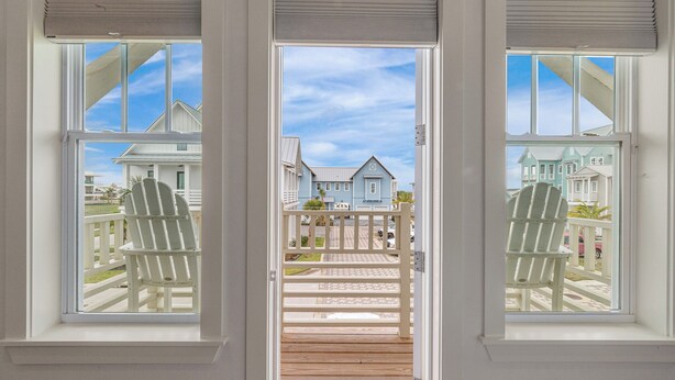 A view from a window with a wooden deck leading to a porch, overlooking houses and a clear sky. - SBS700 Shared Resort Style Pools, Boardwalk to the Beach, Charcoal Grill (Port Aransas)