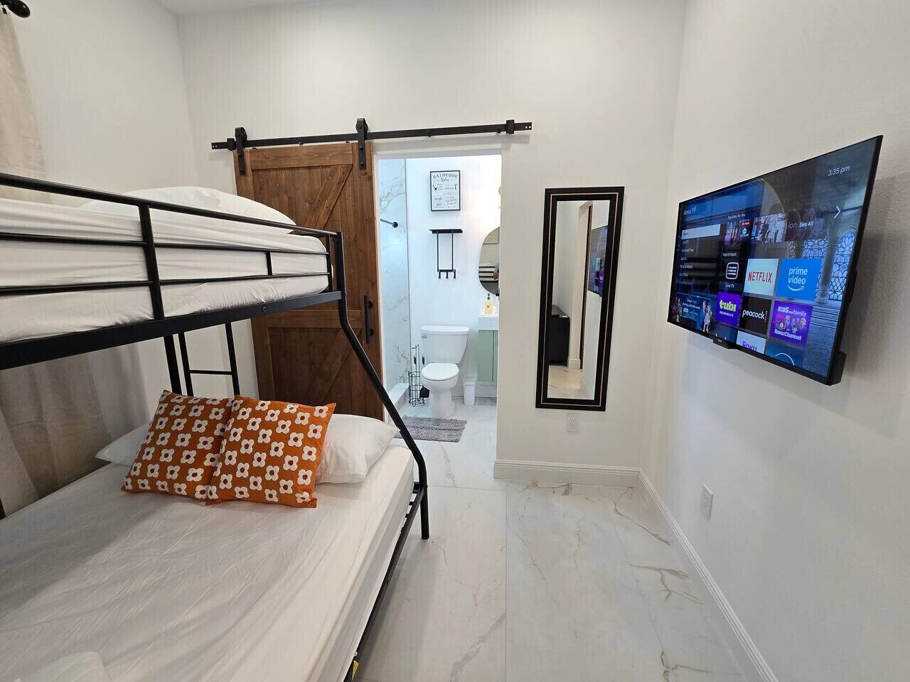 Een slaapkamer met stapelbedden, een televisie en een badkamer die door een open deur zichtbaar is.