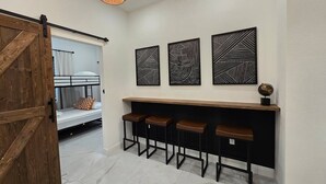 Un corridoio con una porta in legno, una panca con degli sgabelli e tre opere d'arte astratte a parete.