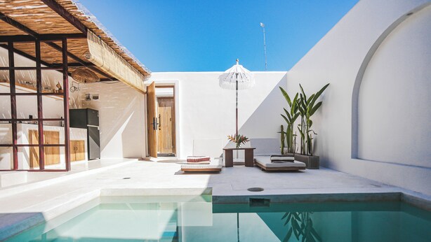 Un área de piscina moderna con una piscina cristalina, una puerta de madera y una pared blanca con una planta.