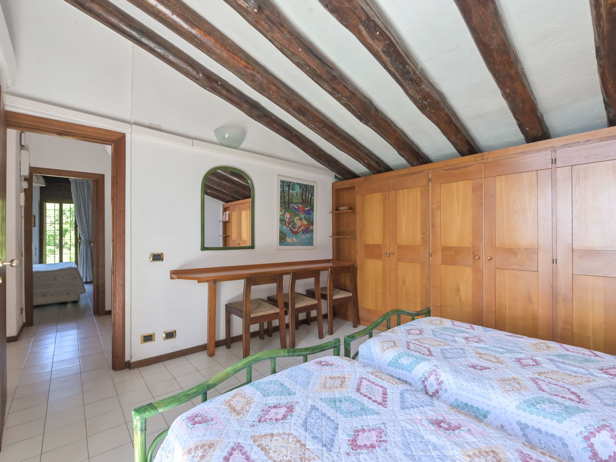 Une chambre avec un lit en bois, un bureau et une armoire. Il y a un miroir sur le mur et un tableau au-dessus du bureau.