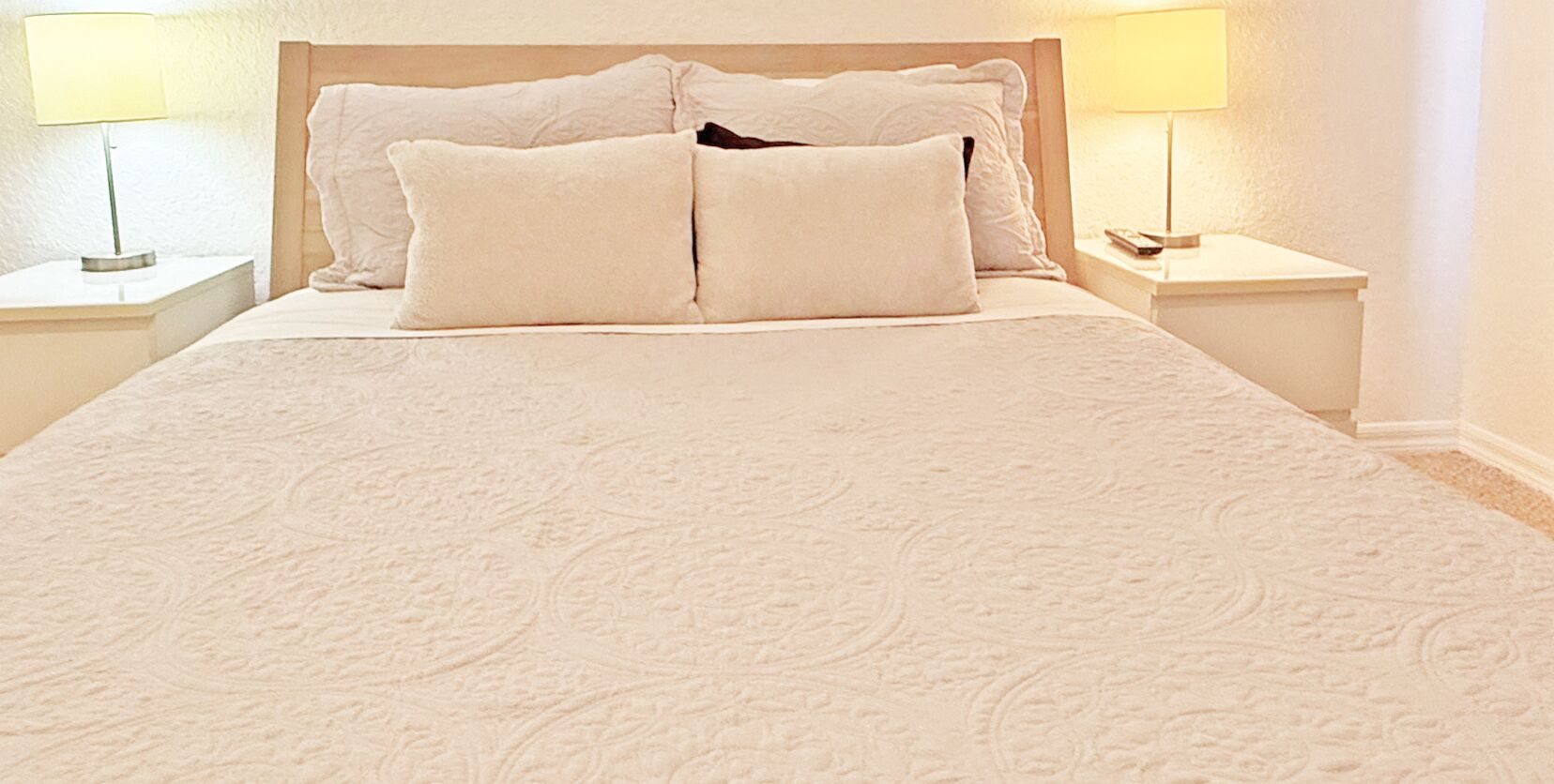 A neatly made bed with a patterned bedspread, two pillows, and two bedside lamps on white nightstands.