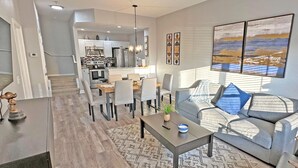 A modern living room with a grey sofa, a coffee table, and a dining area with a chandelier. - Seven Dwarfs Resort -Close to Disney (Kissimmee)