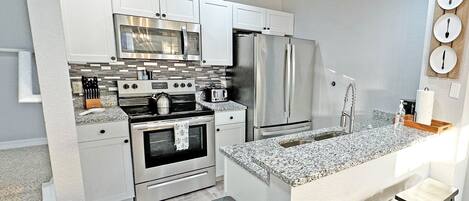 A modern kitchen with white cabinets, stainless steel appliances, a granite countertop, and a bar stool.