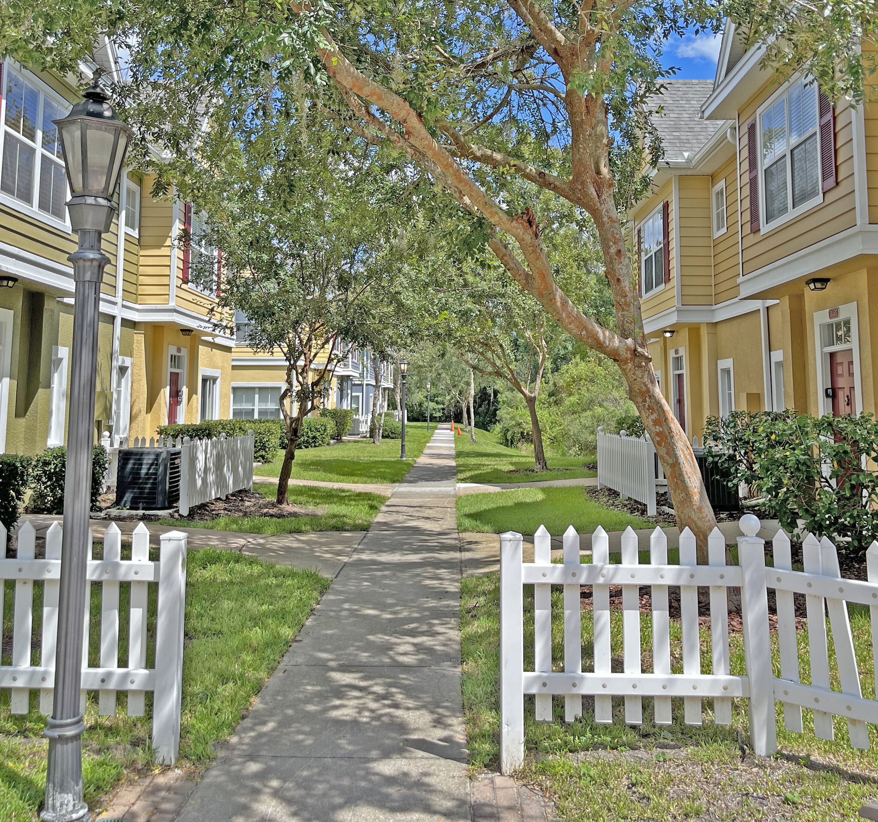 A residential street with yellow houses, white picket fences, and a clear sky.