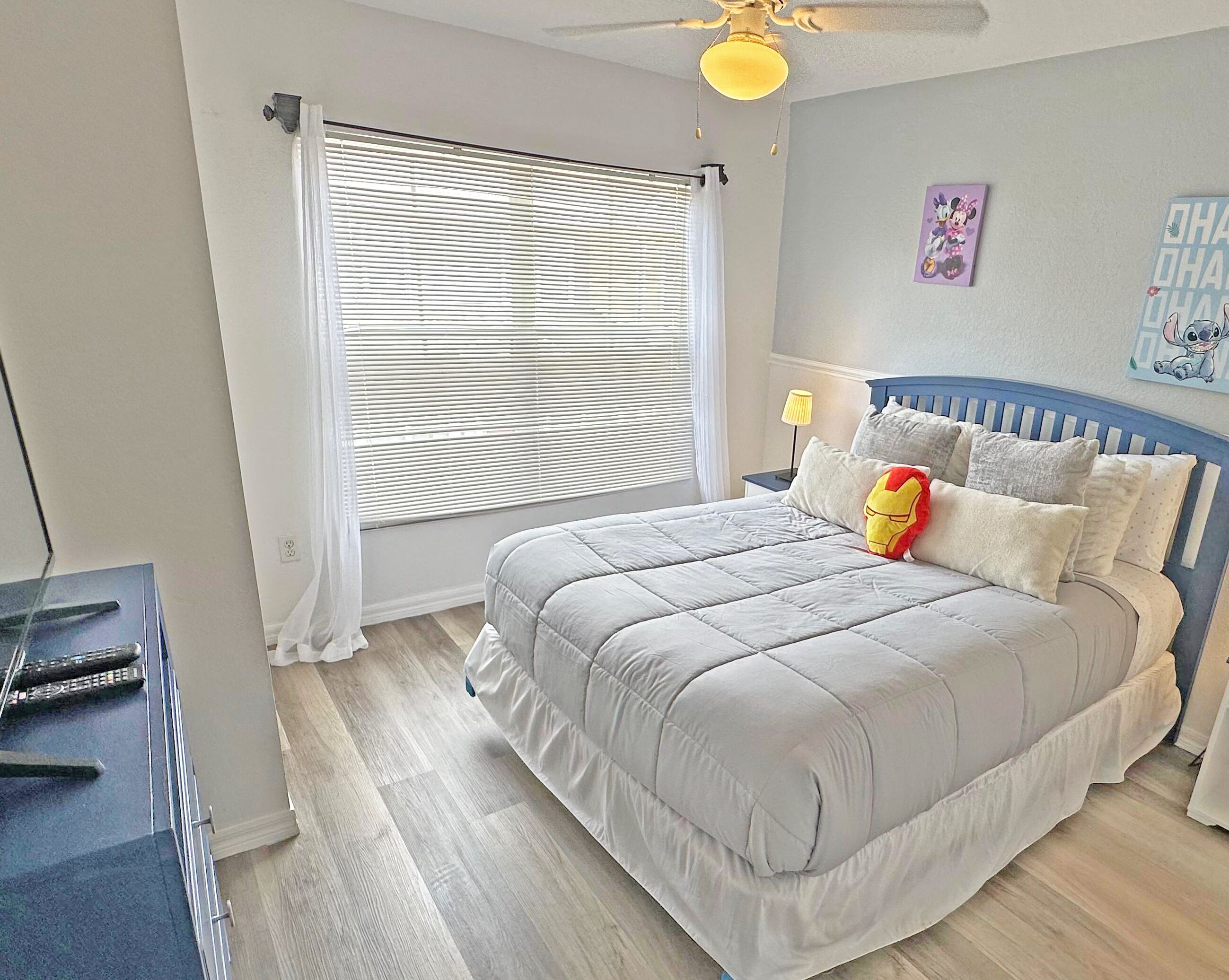 A bedroom with a bed, a nightstand, a lamp, a ceiling fan, and a window with blinds.
