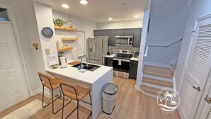 A modern kitchen with a central island, bar stools, a trash can, and a microwave. - Seven Dwarfs Resort -Close to Disney (Kissimmee)