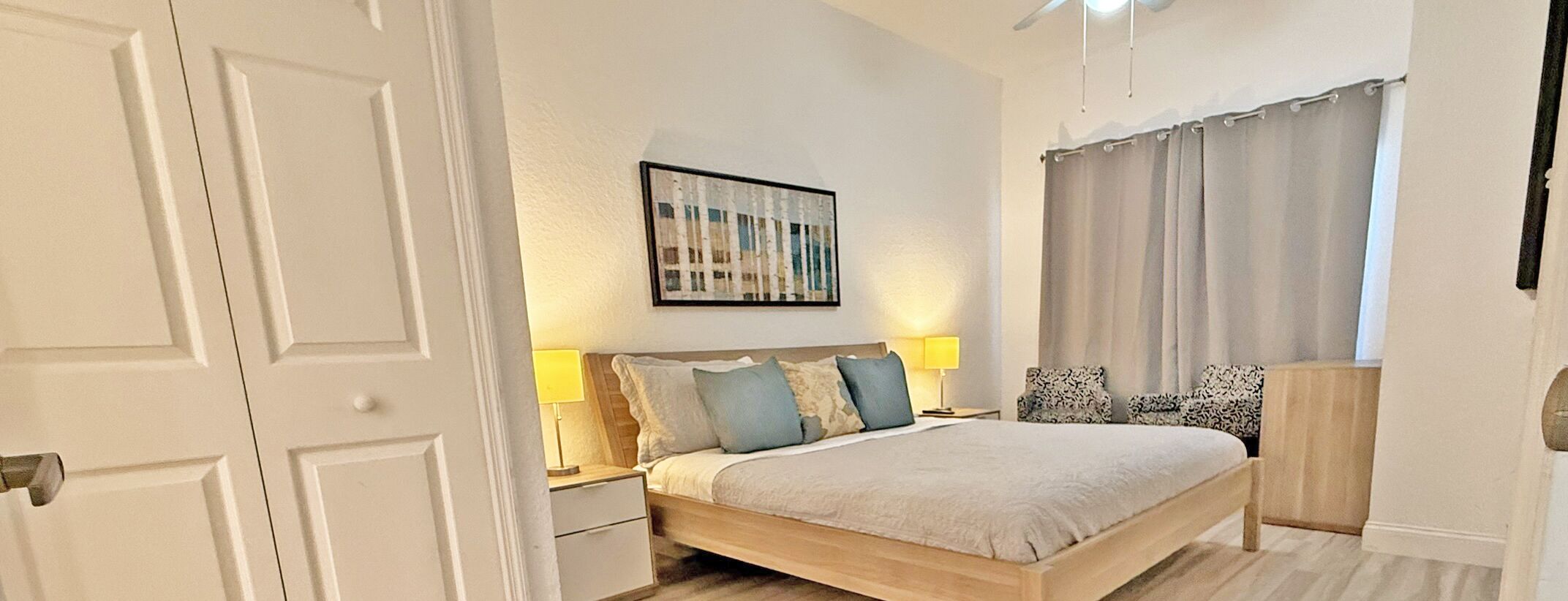 A bedroom with a bed, nightstands, a lamp, a painting, and a window with curtains.