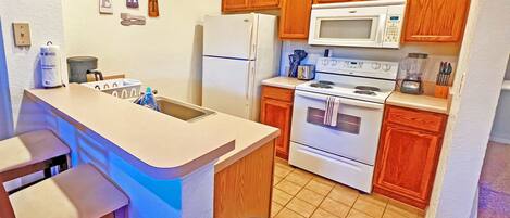 Una cocina con armarios de madera, un refrigerador blanco, un microondas y un horno.