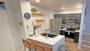 A modern kitchen with a central island, bar stools, a trash can, and a microwave.