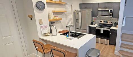 A modern kitchen with a central island, bar stools, a trash can, and a microwave.