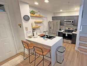 A modern kitchen with a central island, bar stools, a trash can, and a microwave. - Seven Dwarfs Resort -Close to Disney (Kissimmee)