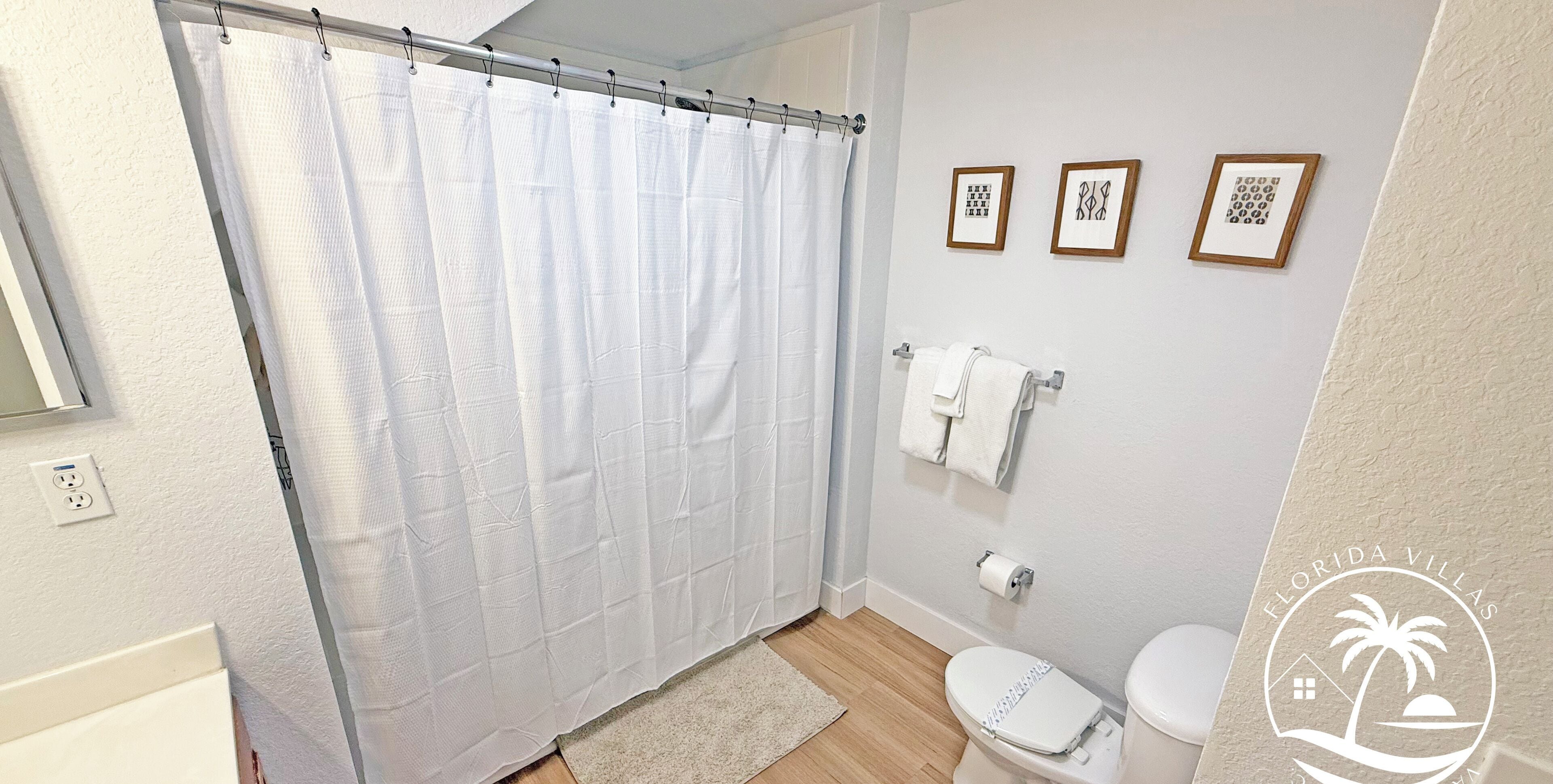 A bathroom with a shower curtain, toilet, and three framed pictures on the wall.