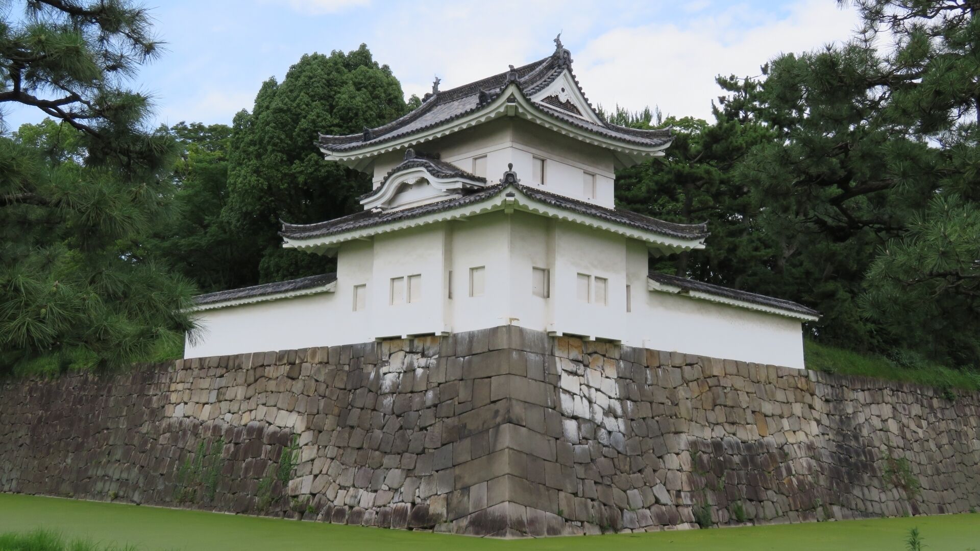 A traditional Japanese castle with a white main building and a stone base, surrounded by trees.