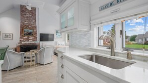 Una cocina con encimera blanca, pileta de acero inoxidable y pared de ladrillo. Hay un letrero sobre la pileta que dice "SEASIDE RETREAT".