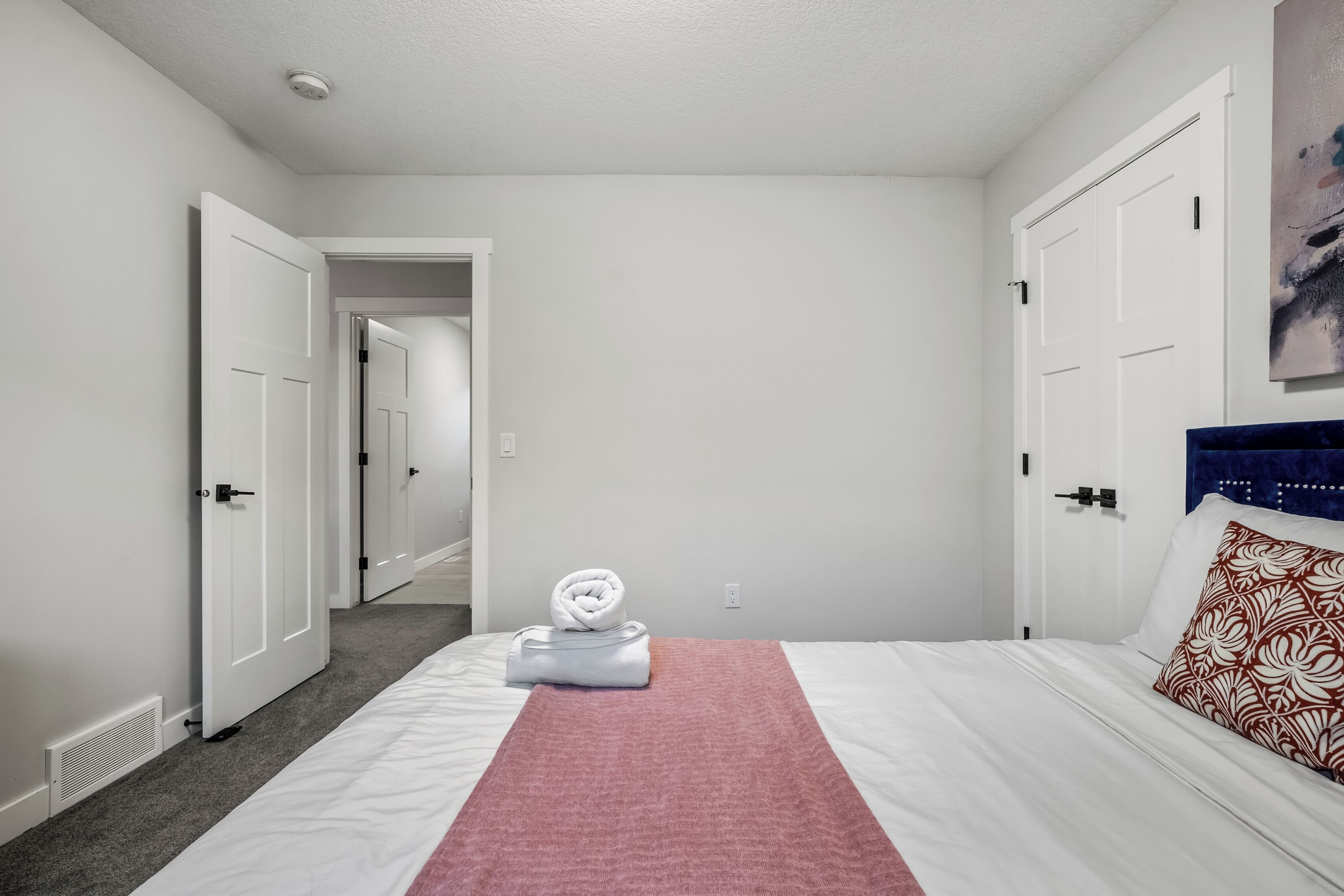 Una camera d'albergo con un letto rifatto, una coperta rosa e un asciugamano sul letto.