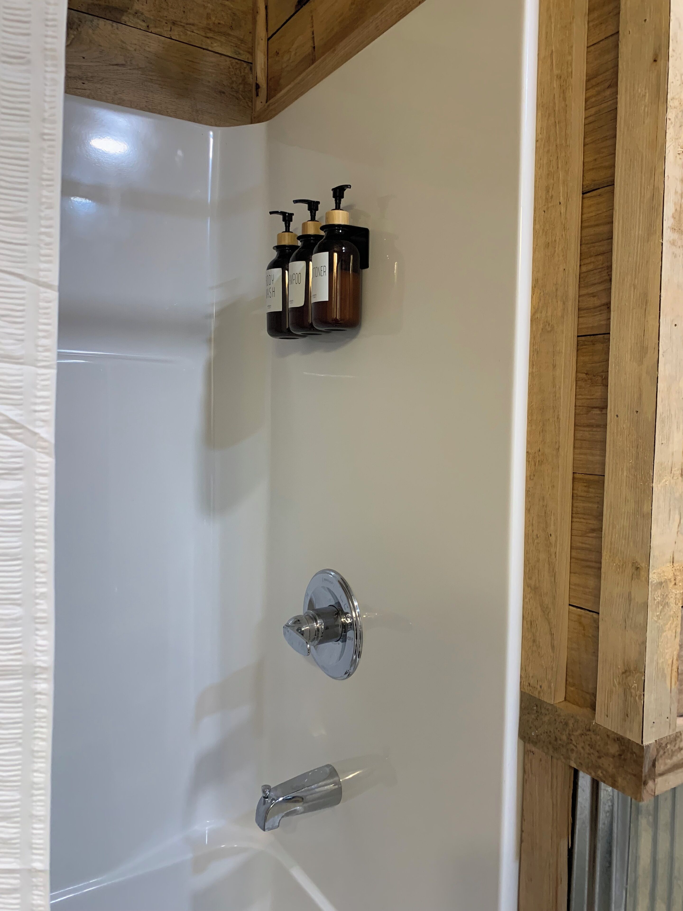 Eine Wanne mit chromfarbenem Wasserhahn und Duschkopf, sowie drei Toilettenartikeln an der Wand.
