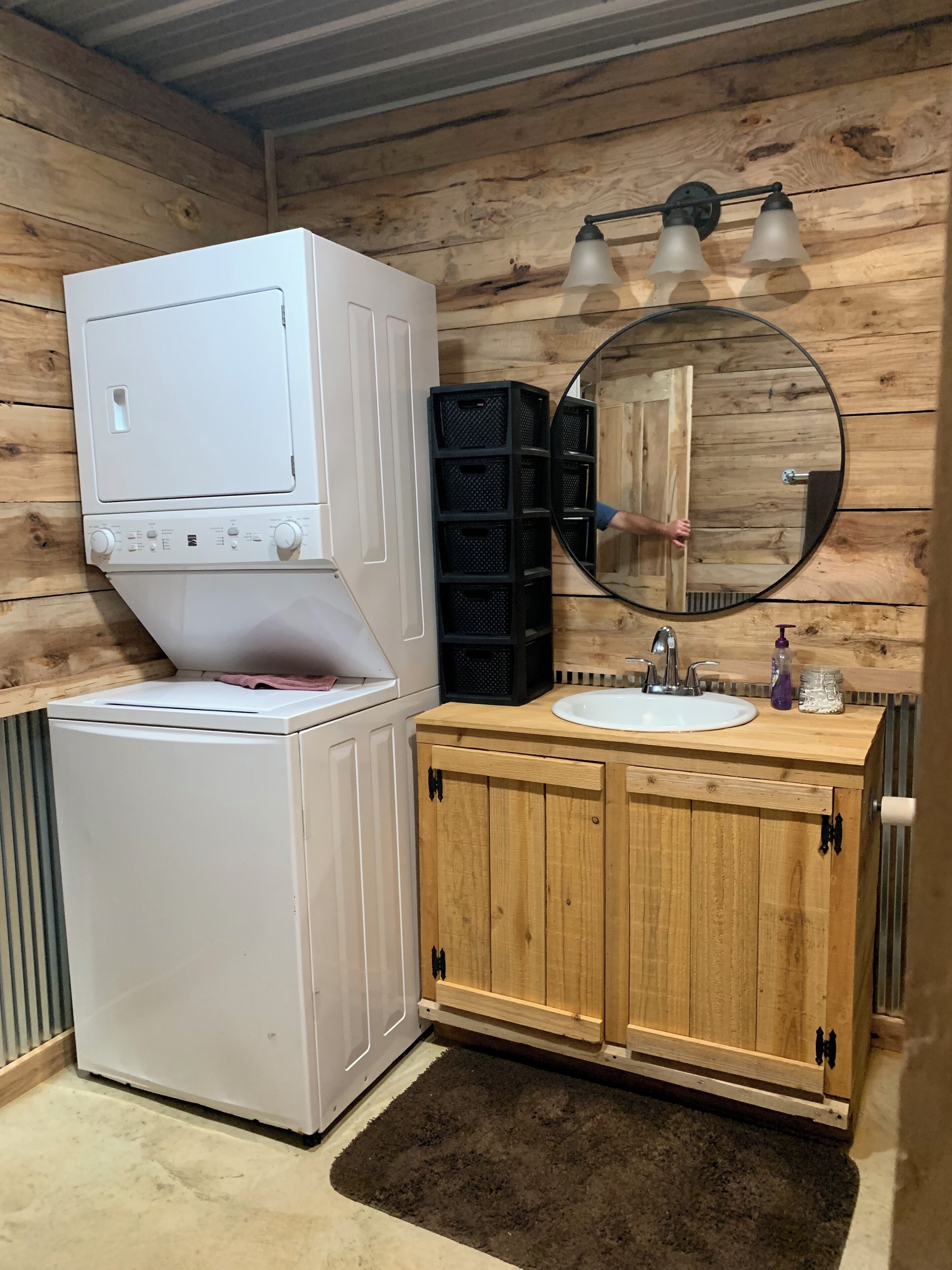 Un bagno compatto con una lavatrice bianca, un mobiletto in legno con lavabo e uno specchio con tre luci.