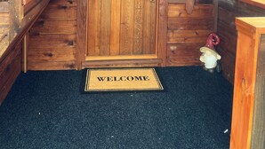 L’entrée d’un chalet en bois, avec une porte ornée d’une guirlande, un paillasson et une petite décoration représentant un gnome.