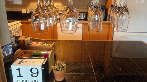 Une cuisine avec des verres à vin suspendus, un calendrier et une plante en pot.