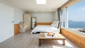 A bedroom with a bed, a wooden nightstand, a dresser, a mirror, and a view of the sea. - The Sea Angler's Pension in Namhae (Namhae)
