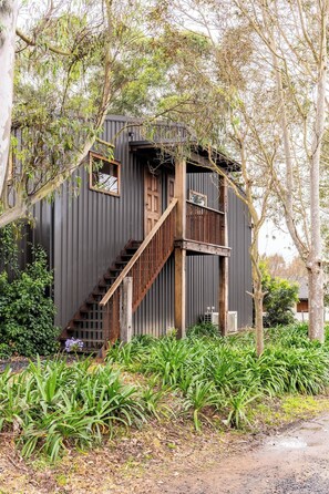 Un rustico chalet con una scala in legno che conduce a un balcone, immerso nel verde.