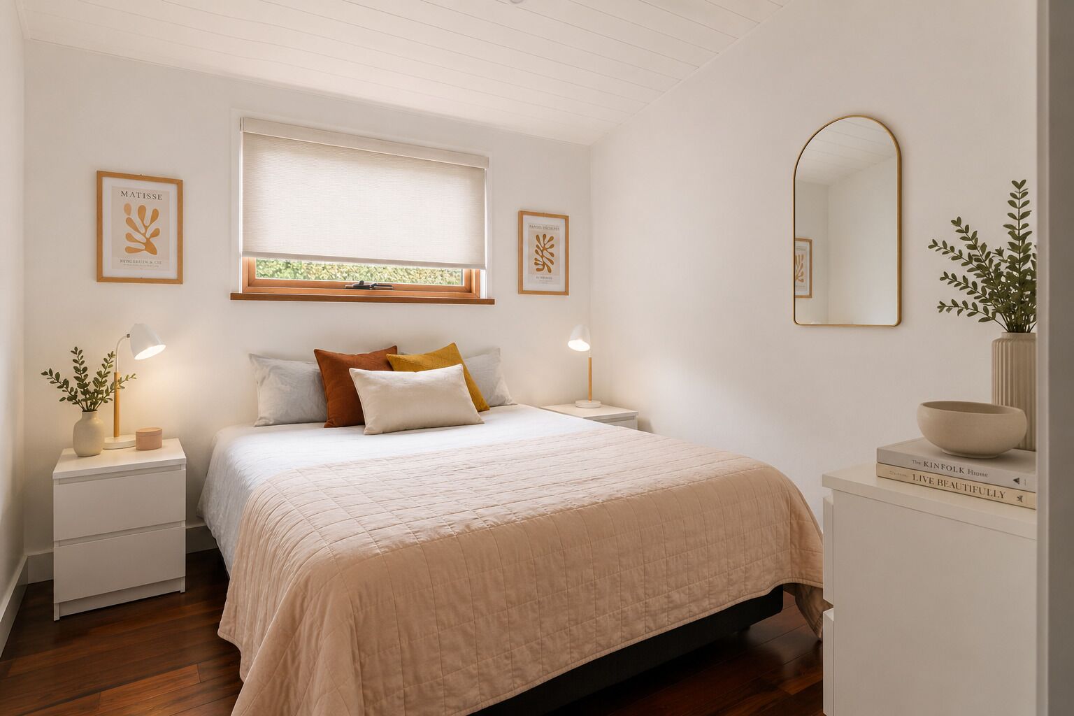A bedroom with a bed, nightstands, a window with blinds, a mirror, and framed artwork on the walls.