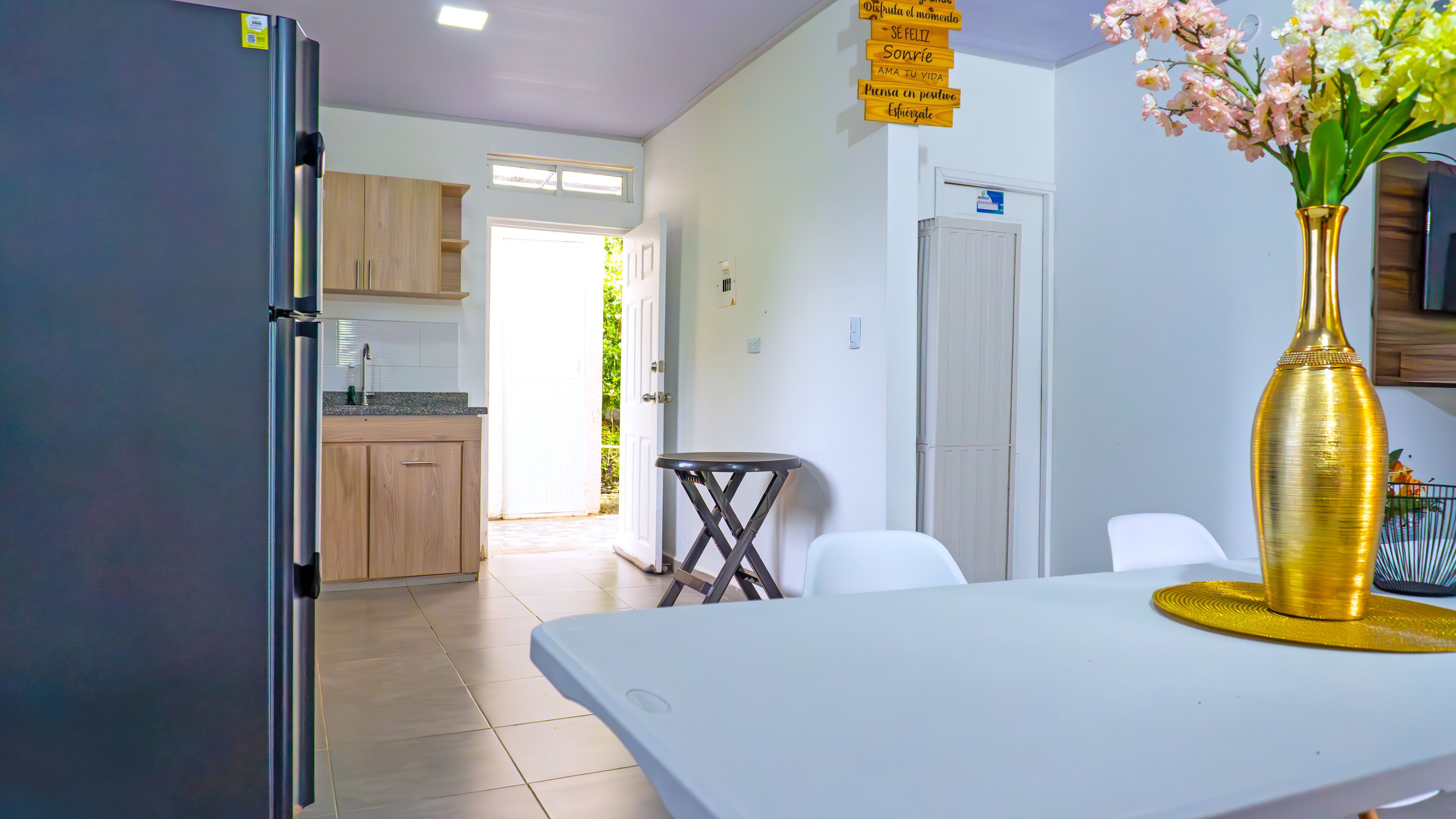 Una cocina moderna con refrigerador, armarios de madera y un comedor con mesa y sillas blancas.