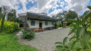 A modern house with a covered porch, surrounded by a gravel driveway and lush greenery. - Chalet - private family estate near Parque del Café - Coffee Region. (Quimbaya)