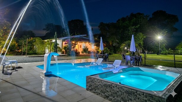 A swimming pool with a water fountain feature, surrounded by lounge chairs and umbrellas. - Chalet - private family estate near Parque del Café - Coffee Region. (Quimbaya)