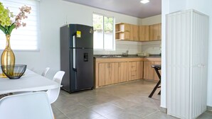 A modern kitchen with a black refrigerator, wooden cabinets, a dining table with chairs, and a vase of flowers. - Chalet - private family estate near Parque del Café - Coffee Region. (Quimbaya)