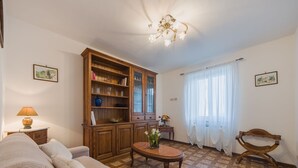 A living room with a sofa, a wooden cabinet, a table with flowers, and a chandelier. - Apartment Viola by Interhome (Gello)